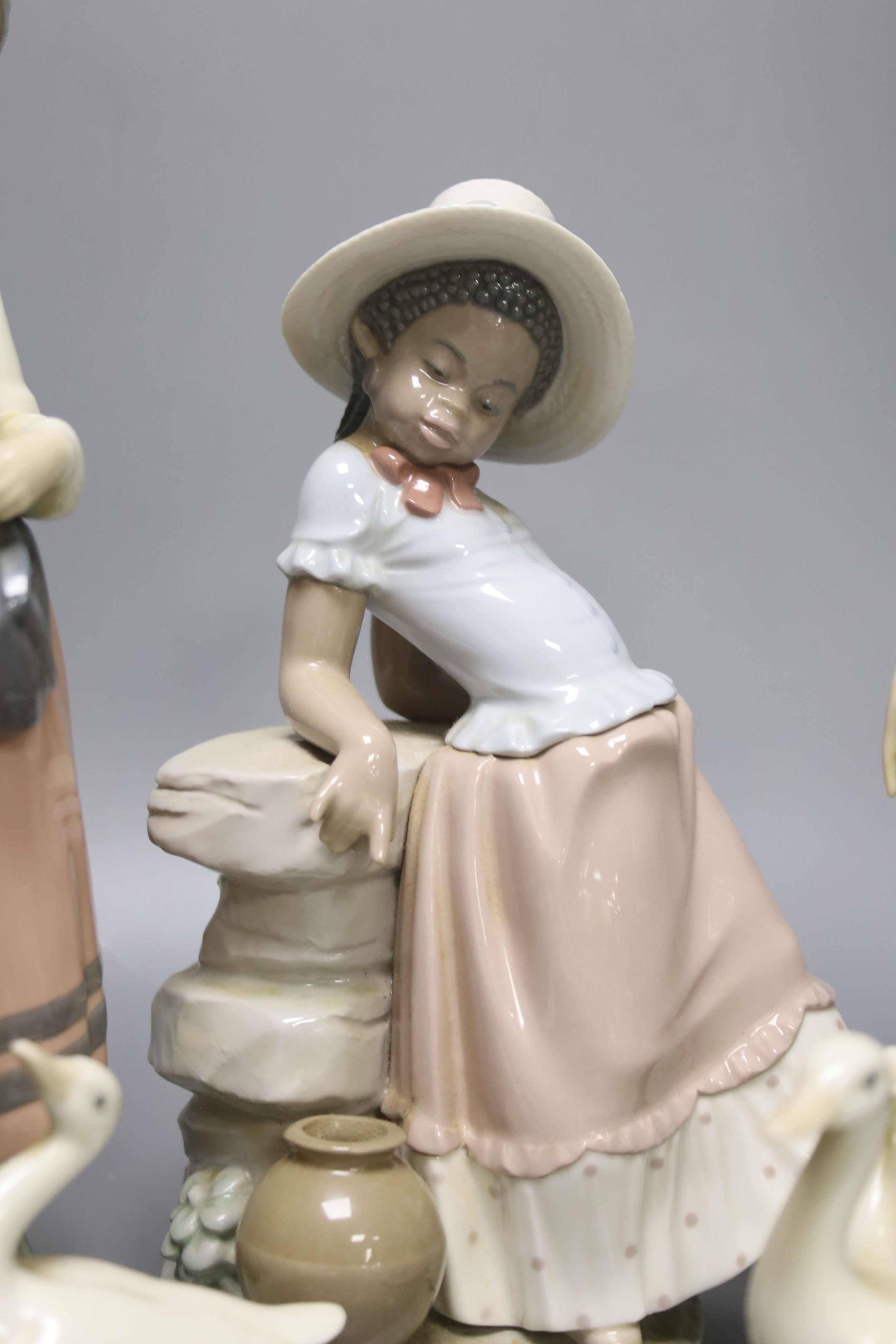 A Lladro figure of a girl feeding a duck, another sitting on a wall, and a girl with two ducks, tallest 26cm